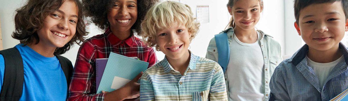 Happy diverse junior school students children group looking at camera standing in classroom. Smiling multiethnic cool kids boys and girls friends posing for group portrait together.